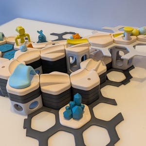 May include: A wooden building block set with various shapes and colours. The set includes light brown, black, grey, and blue blocks, along with small figurines. The blocks are arranged on a grey, honeycomb-shaped base.