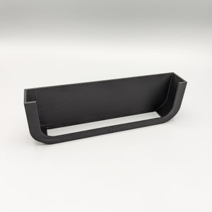 Può includere: Uno scaffale in plastica nera con un bordo curvo. Lo scaffale è progettato per essere montato a parete.