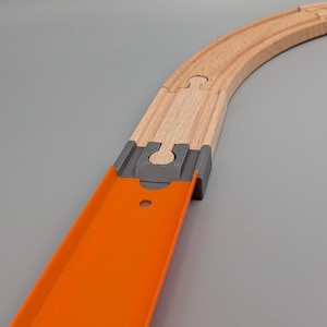 Könnte beinhalten: Ein gebogenes Spielzeug-Eisenbahngleis aus Holz mit einem grauen Kunststoffverbinder und einer orangefarbenen Kunststofframpe. Die Strecke besteht aus hellbraunem Holz und ist für Spielzeugautos oder -züge konzipiert. Die Rampe ist leuchtend orange.