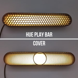 Peut inclure: Gros plan d'un éclairage Philips Hue Play Bar avec un cache en forme de nid d'abeille. La lumière est allumée et éclaire le cache. Le texte "HUE PLAY BAR COVER" est imprimé sous la lumière.