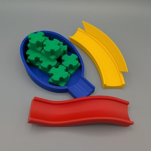 Könnte beinhalten: Ein farbenfrohes Spielzeugset mit einem blauen Behälter voller grüner Puzzleteile, einer roten Rutsche und zwei gelben gebogenen Bahnen. Die Teile sind so konzipiert, dass sie zusammenpassen, was auf ein Lernspielzeug hindeutet.