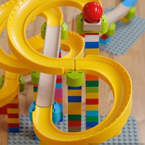 Könnte beinhalten: Ein farbenfrohes Murmelbahn-Spielzeug mit gelben Kunststoffbahnen, Holzrampen und einer roten Murmel. Die Stützen bestehen aus gestapelten, bunten Blöcken. Das Spielzeug ist für Kinder zum Bauen und Spielen konzipiert.