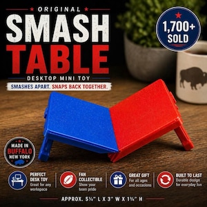 Könnte beinhalten: Ein rotes und blaues "Smash Table" Desktop-Mini-Spielzeug. Das Spielzeug ist ca. 14 cm L x 7,6 cm B x 4,4 cm H groß. Der Text auf dem Bild lautet "Smashes apart. Snaps back together." und "Made in Buffalo New York."