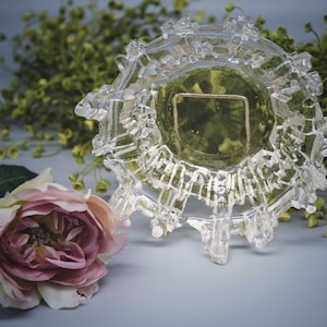 Puede incluir: Un cuenco de vidrio transparente con un diseño geométrico único. El cuenco tiene una forma circular con un borde elevado y texturizado. El cuenco está sobre una superficie gris claro.