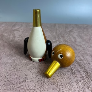 Puede incluir: Dos saleros y pimenteros de madera con forma de pingüino y pájaro. El salero de pingüino es blanco con detalles marrones y rojos y una parte superior dorada. El salero de pájaro es marrón con un pico dorado y ojos blancos.