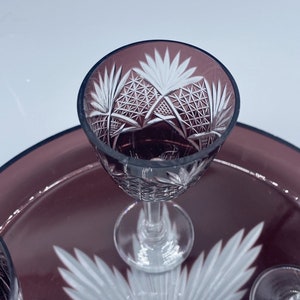 Pu&ograve; includere: Set di quattro bicchieri da shot in vetro trasparente con intricati disegni incisi. I bicchieri sono su un vassoio di colore viola scuro.
