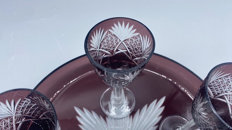 Pu&ograve; includere: Set di quattro bicchieri da shot in vetro trasparente con intricati disegni incisi. I bicchieri sono su un vassoio di colore viola scuro.