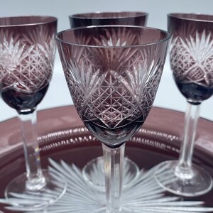 Pu&ograve; includere: Quattro bicchieri da shot in vetro trasparente con un design in vetro tagliato. I bicchieri sono di colore viola scuro e sono su un vassoio con un design a stella.