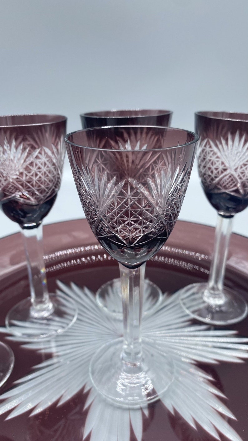 Pu&ograve; includere: Quattro bicchieri da shot in vetro trasparente con un design in vetro tagliato. I bicchieri sono di colore viola scuro e sono su un vassoio con un design a stella.