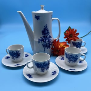 May include: A white coffee pot and four matching cups and saucers with a blue floral design. The cups and saucers have a delicate rim.