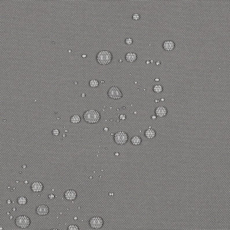 May include: A close-up view of a solid gray fabric surface featuring a tight, woven texture. Numerous clear water droplets are scattered across the material, demonstrating a water-repellent quality as they bead up on the surface.