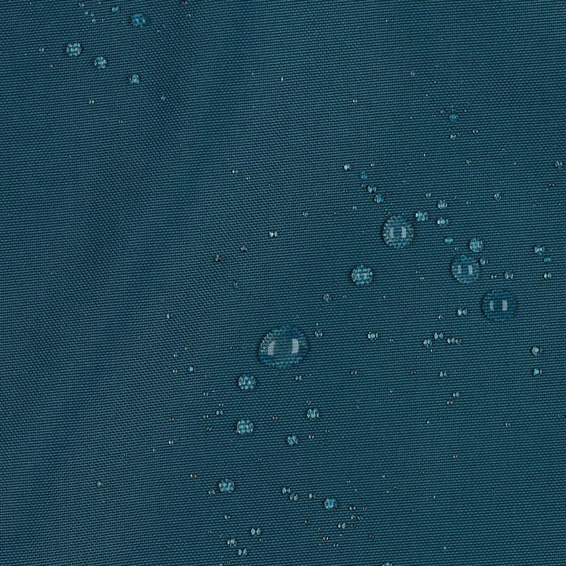 May include: A dark teal fabric surface with a visible woven texture. Numerous clear water droplets of varying sizes are scattered across the material, creating a beaded effect on the surface of the water-resistant textile material.