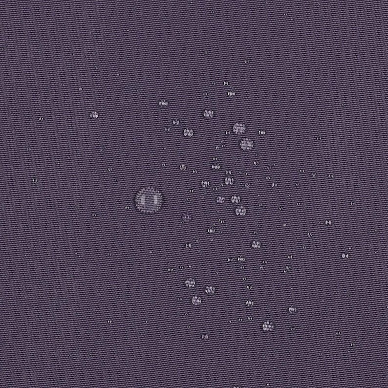 May include: A dark purple fabric surface with a visible woven texture, featuring numerous small, clear water droplets scattered across the material, demonstrating a water-repellent quality on the solid-colored textile.