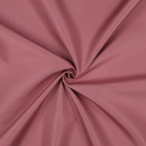 May include: A solid dusty rose fabric featuring a tight, uniform weave. The material is gathered in the center, creating soft, radiating folds and deep shadows that highlight the smooth, matte texture of the textile surface.