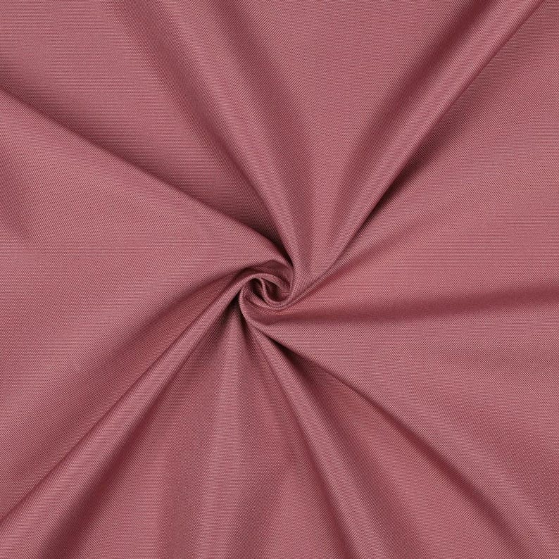 May include: A solid dusty rose fabric featuring a tight, uniform weave. The material is gathered in the center, creating soft, radiating folds and deep shadows that highlight the smooth, matte texture of the textile surface.