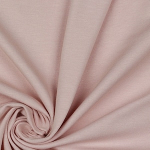 May include: A close-up of a soft, pale pink fabric with a smooth, slightly textured surface. The fabric is folded and draped, creating a gentle, flowing effect.