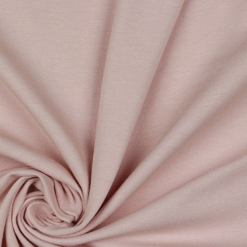 May include: A close-up of a soft, pale pink fabric with a smooth, slightly textured surface. The fabric is folded and draped, creating a gentle, flowing effect.