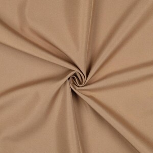 May include: A solid tan fabric with a tight, uniform weave. The material is gathered in the center, creating soft, radiating folds and shadows that highlight the smooth, consistent texture and neutral light brown color of the textile.