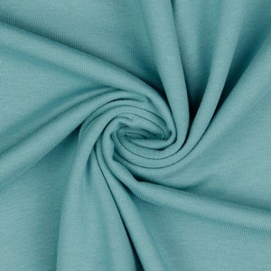 May include: A close-up of a teal blue ribbed fabric. The fabric is folded and twisted, showing the texture of the material.