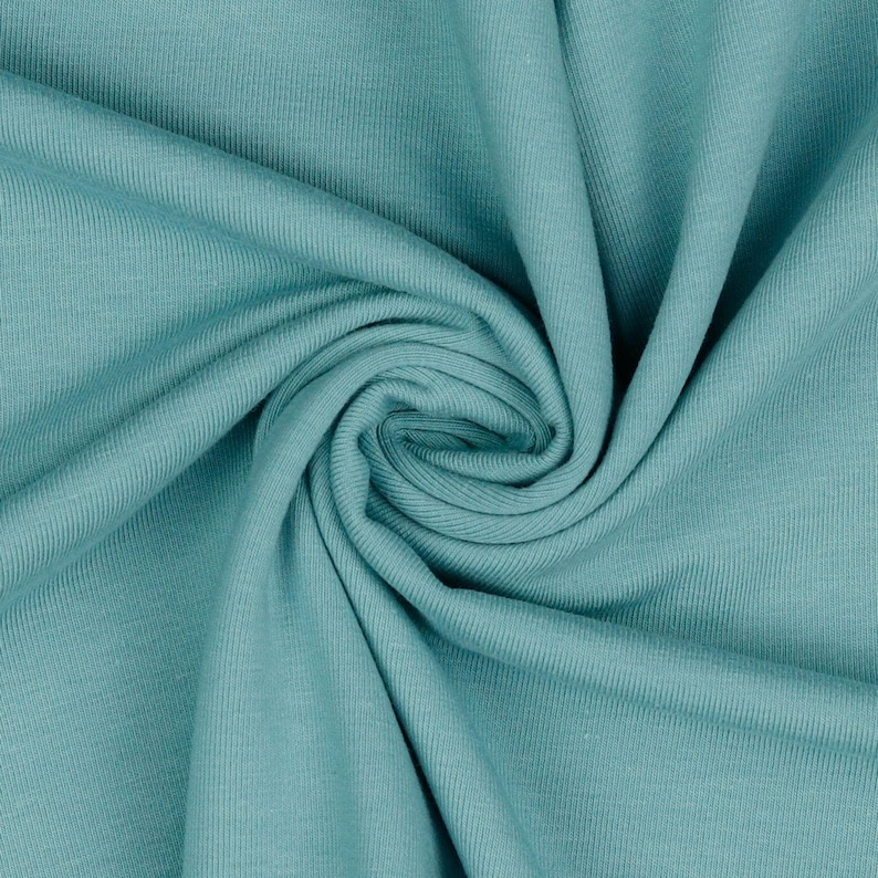 May include: A close-up of a teal blue ribbed fabric. The fabric is folded and twisted, showing the texture of the material.