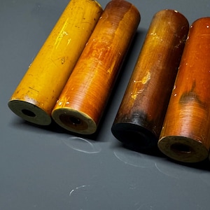 May include: Five wooden dowels in various shades of yellow, brown, and orange. The dowels are all approximately the same length and diameter.