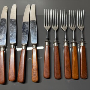 May include: Set of eight vintage silverware pieces, including four knives and four forks. The knives have brown wooden handles and silver blades. The forks have brown wooden handles and silver tines.