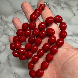 Può includere: Un rosario rosso con un nappa d'argento. Le perle sono di forma ovale e hanno una finitura lucida.