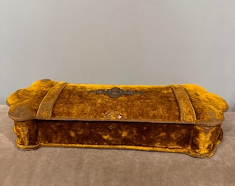 May include: A vintage velvet jewelry box with a gold-colored finish and ornate metal accents. The box has a rectangular shape with rounded edges and a hinged lid.