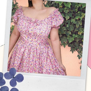 May include: A pink and white floral print dress with a square neckline and short puff sleeves. The dress has a fitted bodice and a flowing skirt.