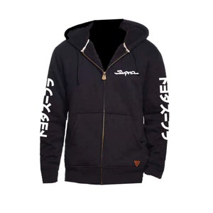 Puede incluir: Sudadera negra con cremallera, logotipo Supra blanco en el pecho y texto japonés blanco en las mangas. El texto en las mangas dice "Supra Gen".