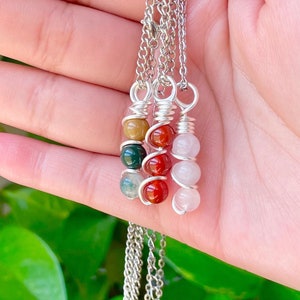 May include: Three silver chain necklaces with gemstone pendants. Each pendant features a different combination of small, round, colorful stones. The stones are wrapped in silver wire.