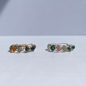 May include: Two wire-wrapped rings with green, orange, and pink stones. The rings are made with gold and silver wire.