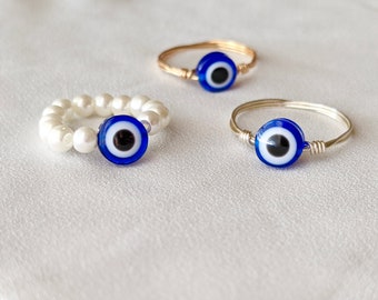 May include: Three evil eye rings. One ring is made of white pearls, one is made of gold wire, and one is made of silver wire. All three rings feature a blue evil eye charm.