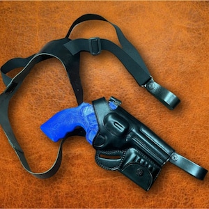 Puede incluir: Una funda de hombro de cuero negro con cinturón a juego y un revólver con mango azul. La funda está diseñada para llevarse sobre el pecho y la espalda. El fondo es de cuero marrón texturizado.