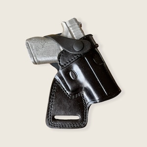 以下が含まれることがあります： ステッチのデザインとベルトループが付いた黒い革製のホルスター。ホルスターの中に銀色の拳銃が入っています。