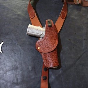 Könnte beinhalten: Ein braunes Lederholster mit einer Pistole darin. Das Holster ist an einem braunen Lederriemen befestigt.