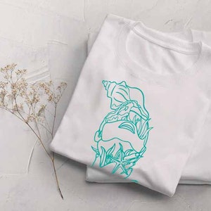 May include: White t-shirt with a teal blue outline of a seashell, starfish, and seaweed design.
