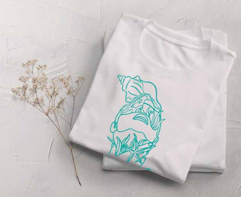May include: White t-shirt with a teal blue outline of a seashell, starfish, and seaweed design.