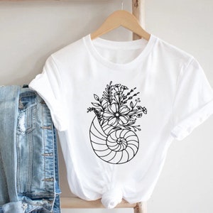 May include: White t-shirt with a black line drawing of a seashell with flowers inside.