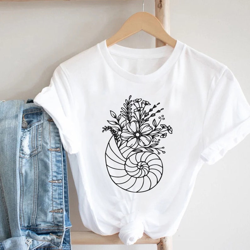 May include: White t-shirt with a black line drawing of a seashell with flowers inside.