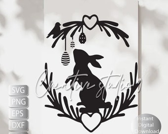 May include: Black and white silhouette of a bunny rabbit with a heart and a bird in a wreath of branches.  The bunny is looking up at a hanging Easter egg.  The image is suitable for crafting projects.