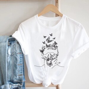 May include: White t-shirt with a black line drawing of a face with butterflies around it.
