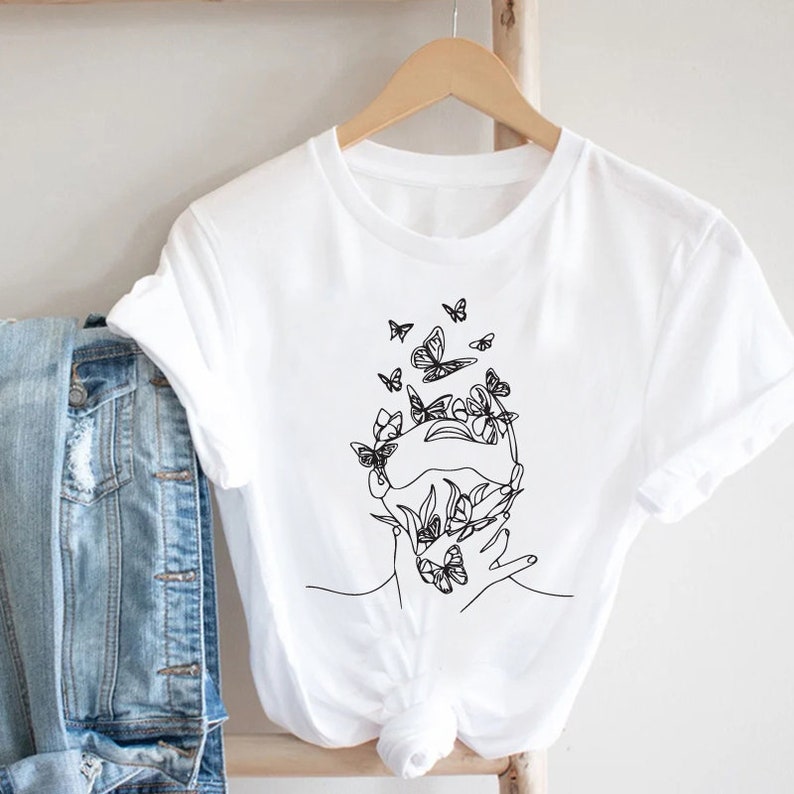 May include: White t-shirt with a black line drawing of a face with butterflies around it.