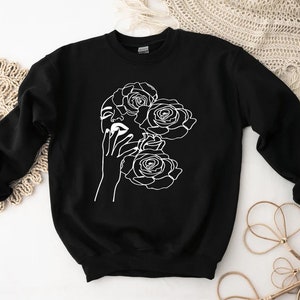 May include: Black sweatshirt with a white line drawing of a woman's face with roses around her head.