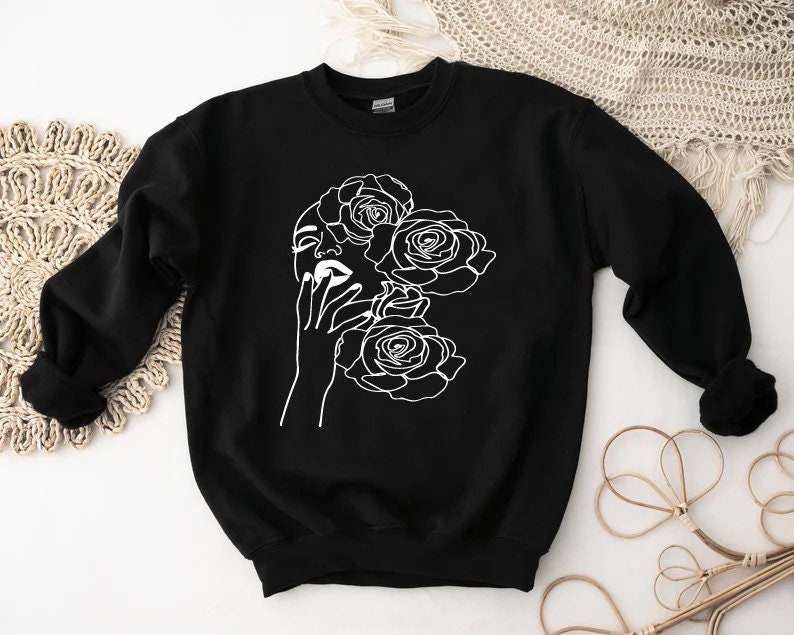 May include: Black sweatshirt with a white line drawing of a woman's face with roses around her head.