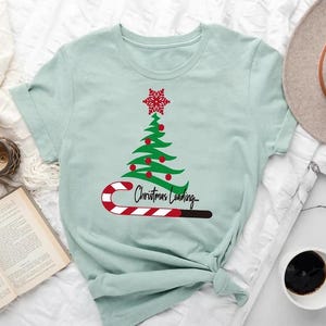 May include: A light blue t-shirt with a green Christmas tree graphic and a candy cane with the text "Christmas Loading..." printed on it.