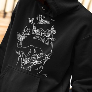 May include: Black hoodie with a white line drawing of hands holding flowers and butterflies.