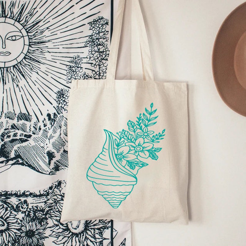 May include: A white canvas tote bag with a teal blue seashell design. The seashell is filled with teal blue flowers and leaves.