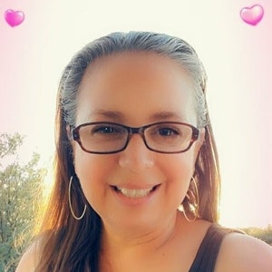 May include: A person smiling, wearing glasses and hoop earrings. They are wearing a black vest top. Pink heart-shaped filters are placed around the image.
