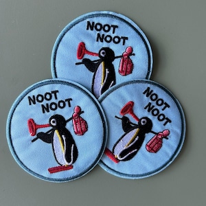 May include: Three embroidered patches with a light blue background and a black border. Each patch features a penguin with a red horn and a red bag, with the words "NOOT NOOT" in black.